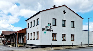 Außenansicht des Firmengebäudes Holz Müller mit weißer Fassade, Firmenlogo und angrenzendem Hof.