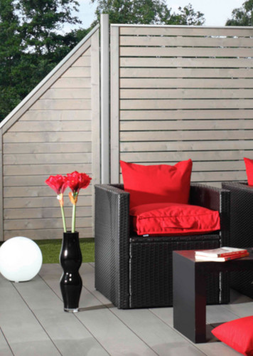 Gartenlounge mit grauem Sichtschutzzaun aus Holz, schwarzen Rattanmöbeln und roten Kissen.