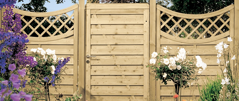 Gartentor mit angrenzenden Holzelementen und Rankgittern in natürlicher Optik, eingerahmt von blühenden Blumen im gepflegten Garten.