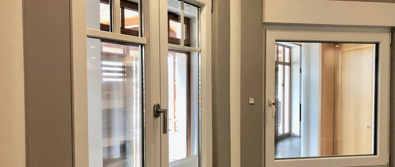 Moderne Fenster in einer Ausstellungssituation – weiße Kunststoffrahmen mit Isolierverglasung in grauer Wand verbaut.