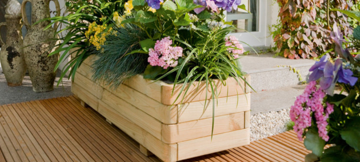 Blumenkästen aus Holz mit farbenfrohen Blumen auf einer Terrasse mit fein gerillten Terrassendielen aus Holz.