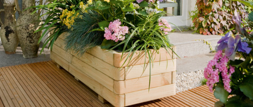 Blumenkästen aus Holz mit farbenfrohen Blumen auf einer Terrasse mit fein gerillten Terrassendielen aus Holz.